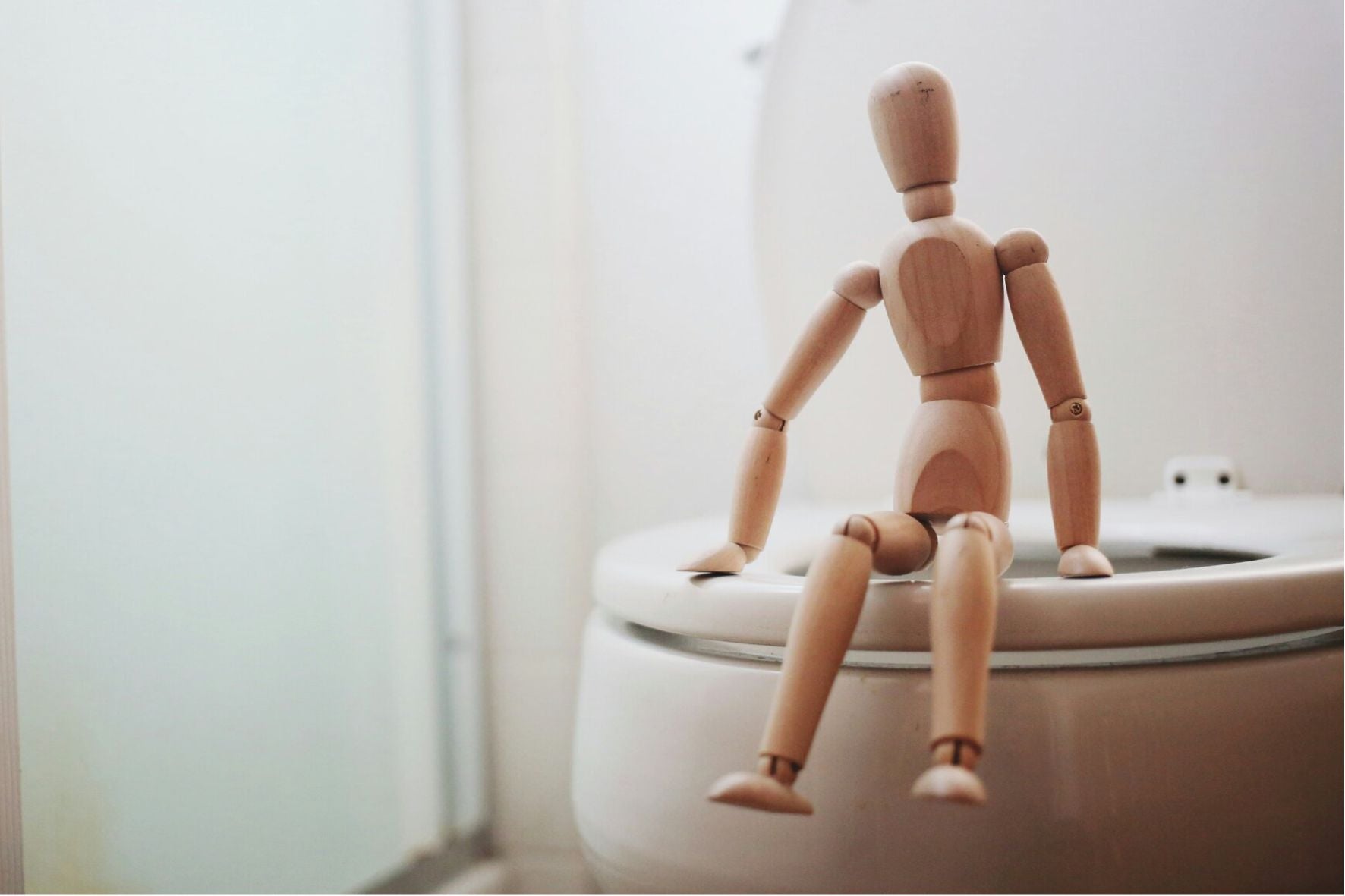 Une figurine articulée en bois assise sur la toilette comme symbole des lochies et des fuites urinaires postpartum.